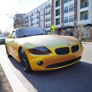 A vibrant yellow BMW sports car parked on a city street, showcasing its sleek design against a backdrop of modern apartment buildings.