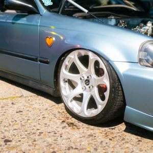 A modified car with a sleek blue exterior and distinctive white alloy wheels, showcasing a lowered suspension and a heart-shaped sticker on the side.