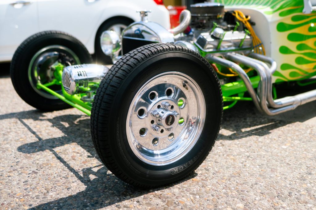 Close-up of a custom car wheel with shiny chrome rims and green flame accents on the body. The setting is a sunny day, conveying a vibrant, energetic mood.