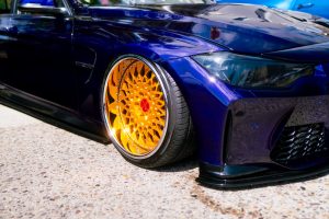 Close-up of a sleek, dark blue sports car with vibrant gold custom rims. The polished body reflects light, conveying luxury and high performance.