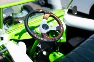 Close-up of a stylish car interior featuring a wooden and black steering wheel, bright green dashboard, and leather seat.