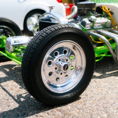 Close-up of a custom car wheel with shiny chrome rims and green flame accents on the body. The setting is a sunny day, conveying a vibrant, energetic mood.