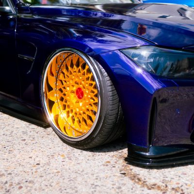 Close-up of a sleek, dark blue sports car with vibrant gold custom rims. The polished body reflects light, conveying luxury and high performance.
