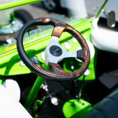 Close-up of a stylish car interior featuring a wooden and black steering wheel, bright green dashboard, and leather seat.